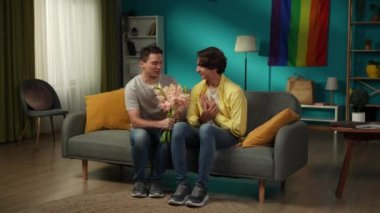 Evde homoseksüel bir çiftin tam boy videosu. Biri elinde çiçek buketi ile çerçeveye girer, bunları partnerine verir, iltifatlar, dileklerle. LGBT, eşitlik, eğitim içeriği.