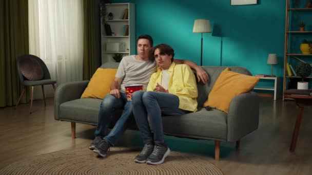 ソファに座っている同性カップルのフルサイズのビデオ 一緒にテレビを見たり ポップコーンを食べたり 彼らの1人はホラー映画を恐れ パートナーは彼らを慰めようとします Lgbt プライド — ストック動画