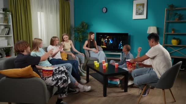 10代 ソファーに座ってテレビを見ている友人 ホラー映画 シリーズ 彼らはポップコーンを食べて しゃべったり 冗談を言ったりしている ティーンエイジャー 若者コンテンツ — ストック動画