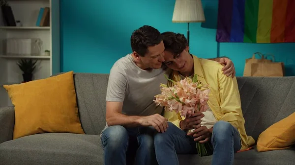 自宅で同性愛者のカップルを撃った 一人はちょうど彼らのパートナーに花束を与え 愛と愛情を表現しました 男たちは優しく抱きしめている Lgbt 教育コンテンツ — ストック写真