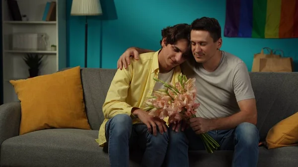 自宅で同性愛者のカップルを撃った 一人はちょうど彼らのパートナーに花束を与え 愛と愛情を表現しました 男たちは優しく抱きしめている Lgbt 教育コンテンツ — ストック写真