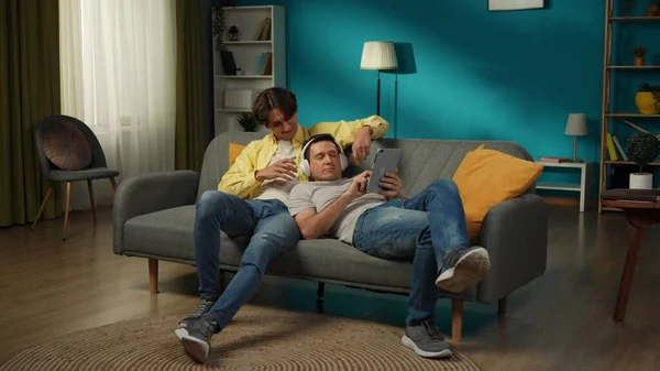 一对同性恋夫妇在家里拍的全景照片他们躺在沙发上 在平板电脑上看照片或录像 一个是共用耳机 Lgbt Equality Educational Content Pride — 图库照片