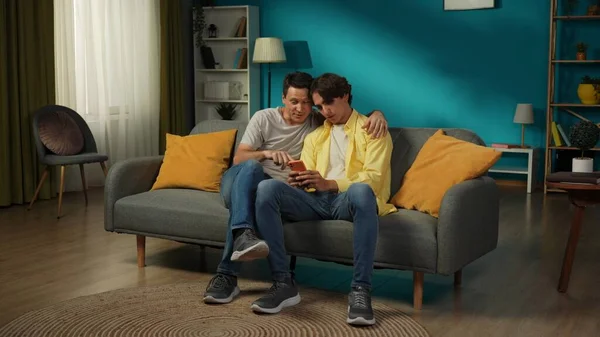 一对同性恋夫妇在家里拍的全景照片他们躺在沙发上 在智能手机上看照片或录像 彼此表达爱意 Lgbt — 图库照片
