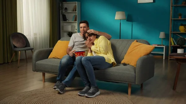 一对同性恋夫妇坐在沙发上看电视和吃爆米花的全景照片 他们中的一个害怕恐怖片 他们的伴侣试图安慰他们 Lgbt — 图库照片