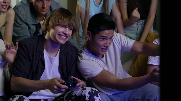 一群青少年 年轻人 朋友们围坐在电视前 站在电视前欢呼 鼓励着两个人 男孩们玩着游戏机 玩游戏 游戏者 青少年 青年内容 — 图库照片