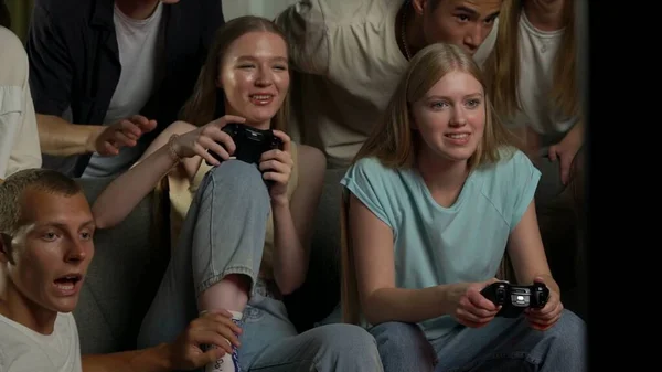 一群青少年 年轻人 朋友们围坐在电视前 站在电视前欢呼 鼓励着两个玩着游戏机 玩游戏 打斗的女孩 游戏者 青少年 青年内容 — 图库照片