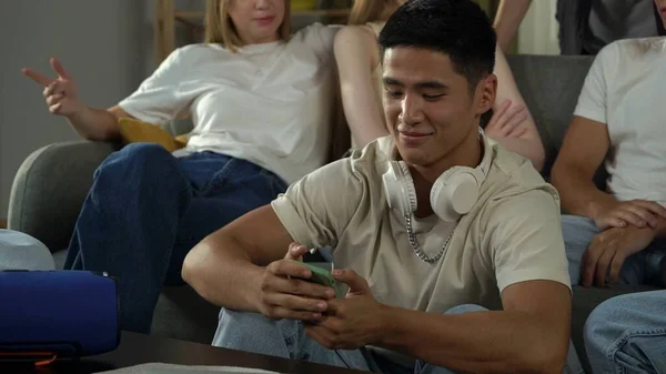 Shot of a boy, guy, sitting in a group of teens, young people, listening to music, scrolling through, surfing the Internet, social media, feed. Advertisement, musical platforms, youth, teenager.