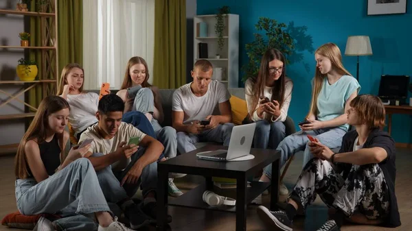 一组青少年 年轻人 坐在沙发上和桌子周围地板上的朋友 用他们的智能手机 笔记本电脑 平板电脑 聊天的全景照片 Gen — 图库照片