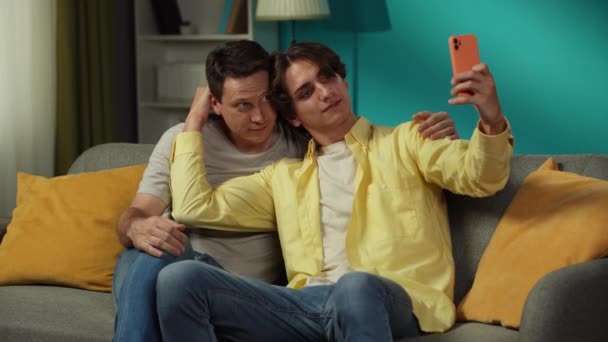 2人の同性愛者のビデオ 自宅でカップル 彼らはソファーに座り 抱きしめ セルフィーを撮り 幸せに話し合っています Lgbt 教育コンテンツ プライド — ストック動画