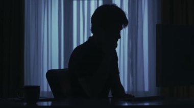 Karanlık dairedeki erkek siluetinin portresi. Günlük yaratıcı yaşam konsepti. Adam evde bilgisayar başında çalışıyor, belgeleri okuyor, telefon alıyor, iş arkadaşıyla telefonda gergin bir konuşma yapıyor.