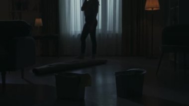 Karanlık dairedeki kadın siluetinin portresi. Günlük yaratıcı yaşam konsepti. Kadın telefonda birini arıyor, tartışıyor. Yerde rulo halı ve kova dolusu su var..