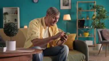 Evdeki kanepede otururken akıllı telefon kullanan bir adam. Adam sosyal medya hesaplarını karıştırıyor, fotoğraflara bakıyor, görüntüyü büyütüyor ve anılarını anlatırken gülüyor. Konsept