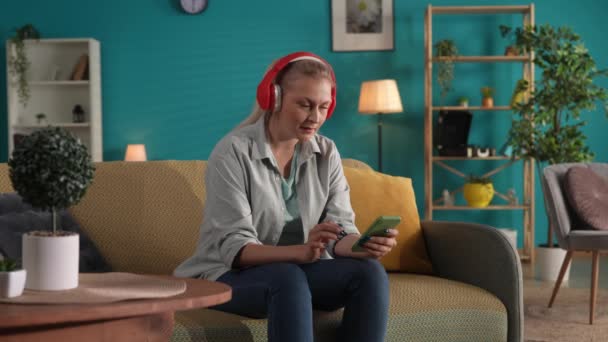 Жінка Червоних Бездротових Навушниках Вибирає Музику Списку Своєму Смартфоні Вмикає — стокове відео