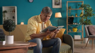 Adam evde kanepede otururken kitap okuyor. Aile mutluluğu, rahatlık, evde dinlenme.