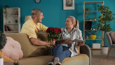 Sürpriz hazırlıyorum. Bir adam elinde tabletle kanepede oturan bir kadına bir buket kırmızı gül sunar. Yıldönümü, Kadın Günü, Sevgililer Günü