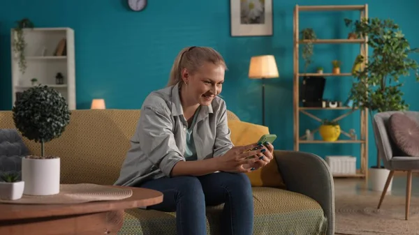 Bir Kadın Evdeki Kanepede Otururken Akıllı Telefon Ekranına Gülümseyerek Bakıyor — Stok fotoğraf