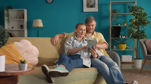 一男一女看着平板电脑上的照片和视频 一对已婚夫妇坐在客厅沙发上拥抱的画像 家庭田园诗 — 图库照片