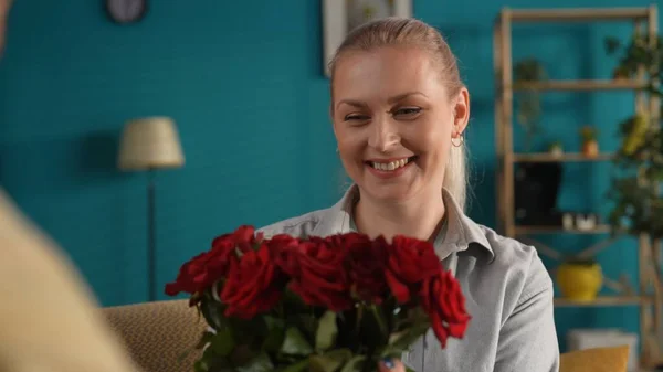 A woman receives a bouquet of red roses as a gift from a man. Portrait of a young woman in the living room with a bouquet of flowers. Anniversary, Womens Day, Valentines Day