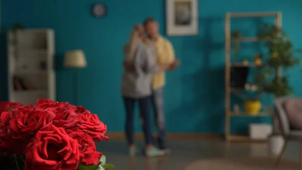 A bouquet of red roses close up on a blurred background of a dancing couple. A man and a woman are dancing in the living room. Date, anniversary, womens day, Valentines day