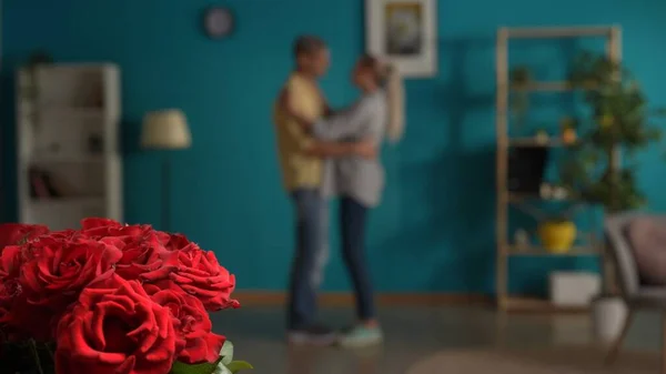 A bouquet of red roses close up on a blurred background of a dancing couple. A man and a woman are dancing in the living room. Date, anniversary, womens day, Valentines day