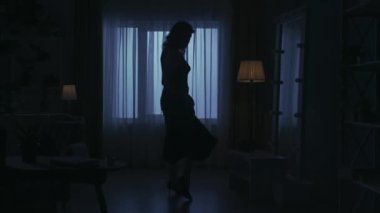 Karanlık dairedeki kadın siluetinin portresi. Günlük yaratıcı yaşam konsepti. Elbiseli ve yüksek topuklu bir kadın bir odaya girer, aynada kendine bakar, randevuya hazırlanır..