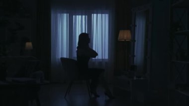Karanlık dairedeki kadın siluetinin portresi. Günlük yaratıcı yaşam konsepti. Odada bir sandalyede oturan, aynaya bakan, saç ve fırçayla makyaj yapan bir kadın..