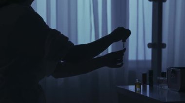 Karanlık dairedeki kadın siluetinin portresi. Günlük yaratıcı yaşam konsepti. Bornozlu kadın odada bir sandalyeye oturmuş, masadan bir şişe tırnak cilası alıyor ve şöyle yapmaya başlıyor: