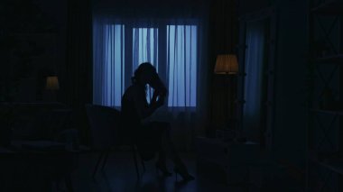 Karanlık dairedeki kadın siluetinin portresi. Günlük yaratıcı yaşam konsepti. Odada bir sandalyede oturan, aynaya bakan, saçını fırçayla düzelten bir kadın..