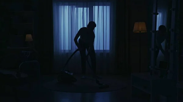 Portrait of female silhouette in the dark apartment room. Everyday life creative concept. Woman in casual clothing vacuuming the carpet in the living room.