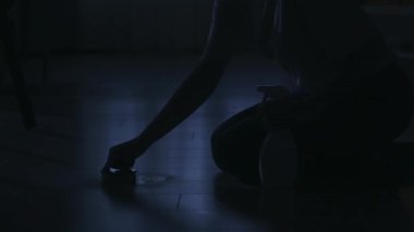 Karanlık dairedeki kadın siluetinin portresi. Günlük yaratıcı yaşam konsepti. Odadaki kadın günlük kıyafetleriyle yerdeki bir şişeden temizleyici püskürtüyor ve fırçayla yıkıyor..