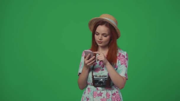旅行广告创意的概念 头戴草帽的女旅行者在智能手机上看到了有趣的东西 脸上带着惊讶的表情 手里拿着钞票 面带微笑 被绿色背景隔离 — 图库视频影像