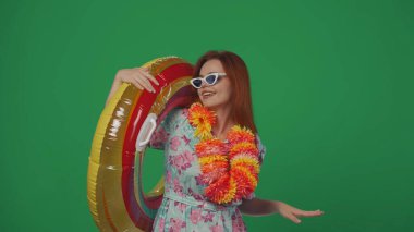Gezici reklam yaratıcı konsepti. Gözlüklü ve çiçek çelenkli bir kadın omzunda şişme tüp halkayla kameraya gülümsüyor. Yeşil arkaplanda izole.
