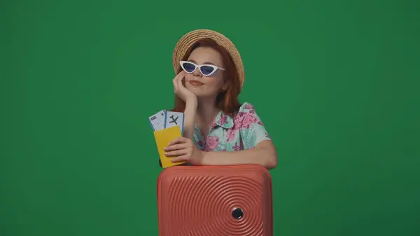 旅行广告创意的概念 头戴草帽 戴着眼镜 提着机票 面带微笑地抬起头的女旅客 被绿色背景隔离 — 图库照片