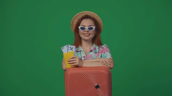 旅行广告创意的概念 头戴草帽 戴着眼镜 提着机票 面带微笑的女旅客 被绿色背景隔离 — 图库照片