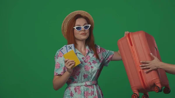 旅行广告创意的概念 戴着草帽和眼镜的女旅客拿着手提箱和机票 满脸喜色 被绿色背景隔离 — 图库照片