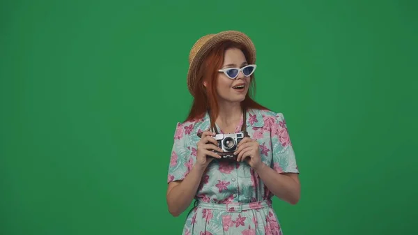 旅行广告创意的概念 戴眼镜 头戴草帽的女人拿着旧胶卷相机 满面春风地环顾四周 被绿色背景隔离 — 图库照片