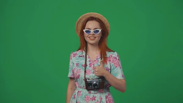 旅行广告创意的概念 戴着草帽和眼镜的女旅行者站在摄像机前 大姆指翘起笑脸 喜形于色 被绿色背景隔离 — 图库照片