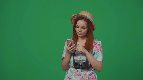 旅行广告创意的概念 戴着草帽的女旅行者拿着智能手机 读着一些有针对性的面部表情的东西 被绿色背景隔离 — 图库照片