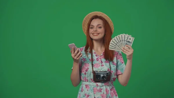 旅行广告创意的概念 头戴草帽的女旅行者拿着智能手机和摇钱树扇子 笑容满面 被绿色背景隔离 — 图库照片