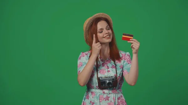 旅行广告创意的概念 头戴草帽的女旅行者拿着银行卡 满脸喜笑地指着它 被绿色背景隔离 — 图库照片