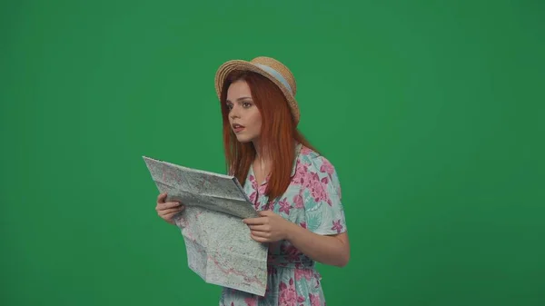 旅行广告创意的概念 头戴草帽 身穿连衣裙的女旅行者拿着纸质地图环顾四周 寻找正确的方向 被绿色背景隔离 — 图库照片