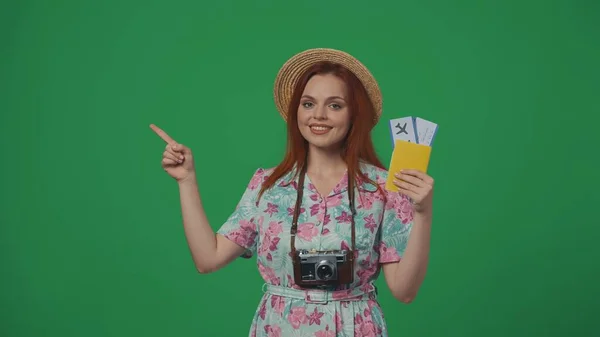 旅行广告创意的概念 戴帽子的女旅客拿着飞机票 指着空旷的地方 微笑着 插入广告的空间 被绿色背景隔离 — 图库照片