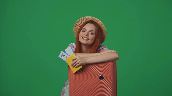 旅行广告创意的概念 头戴草帽的女旅客拿着机票 手放在手提箱上 笑容满面 被绿色背景隔离 — 图库照片