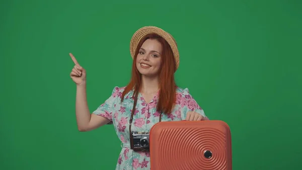 旅行广告创意的概念 头戴草帽的女旅行者拿着手提箱 指着空旷的地方 插入广告的空间 被绿色背景隔离 — 图库照片
