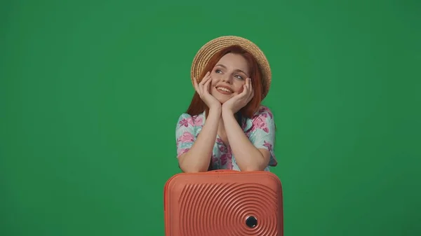 旅行广告创意的概念 头戴草帽的女旅行者 笑容满面 梦想着 手放在手提箱上 被绿色背景隔离 — 图库照片
