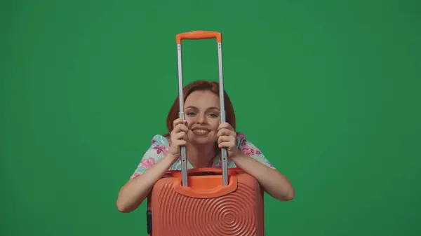 旅行広告クリエイティブコンセプト スーツケースホルダーを通して見る女性旅行者 カメラで笑顔 幸せな顔の表情 緑の背景に孤立した — ストック写真