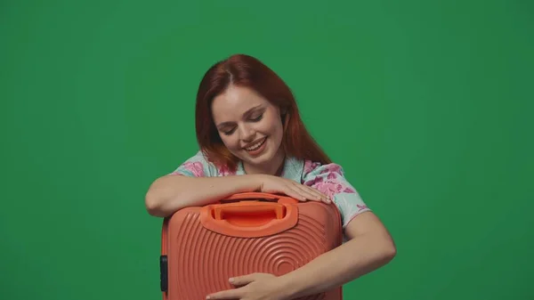 旅行广告创意的概念 穿着漂亮衣服的女旅行者抱着她的橙色手提箱 脸上带着快乐的微笑 被绿色背景隔离 — 图库照片