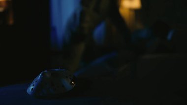 Korku filmi sahnesi. Cadılar Bayramı reklam konsepti. Yakın çekim beyaz hokey maskesine odaklan, sırtından bıçaklı adam manyağı ve koltukta yatan kurban..