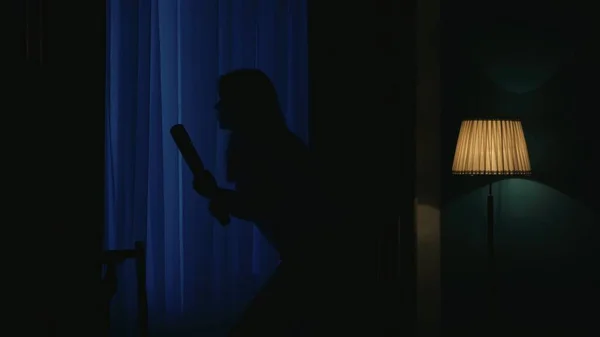 恐怖的电影场景 万圣节广告的概念 在黑暗的公寓客厅里 站在窗边的是一个害怕的小女孩 她拿着棒球棒 — 图库照片