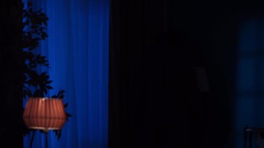 Daire yaratıcı konseptinde korku filmi sahnesi. Karanlık odadaki pencerenin yakın çekimi, dışarıda gök gürültüsü, maskeli adam perdeden çıkar, elinde bıçak olan kameraya bakar.